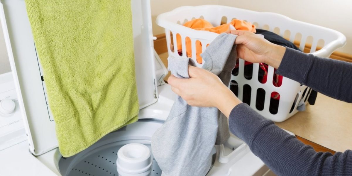Horizontal photo female hands putting dirty laundry into washing machine